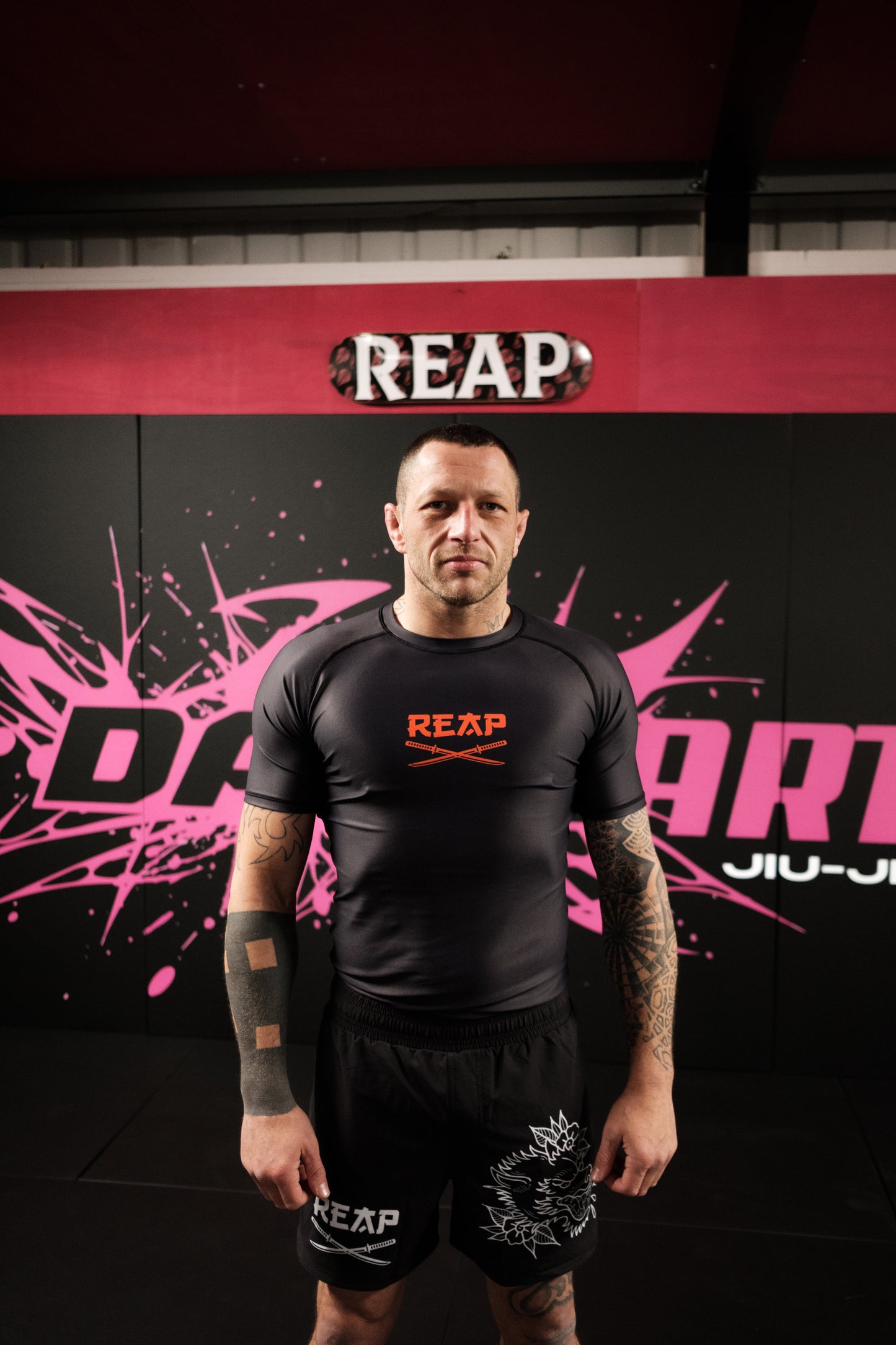 Person wearing a black 'REAP' athletic outfit in front of a red and black background with 'REAP' branding.