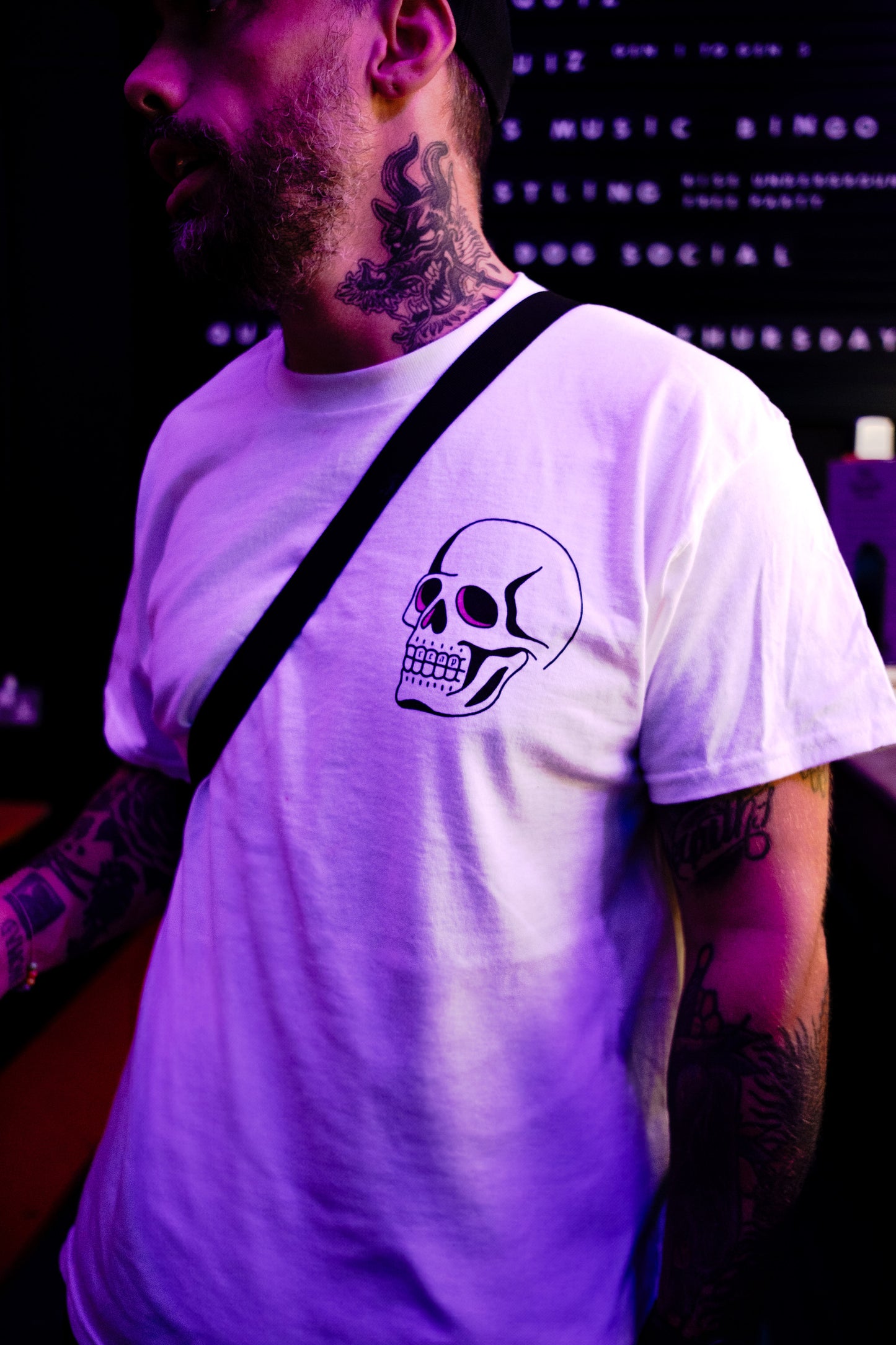 Person wearing a white t-shirt with a skull design, standing against a dark background.