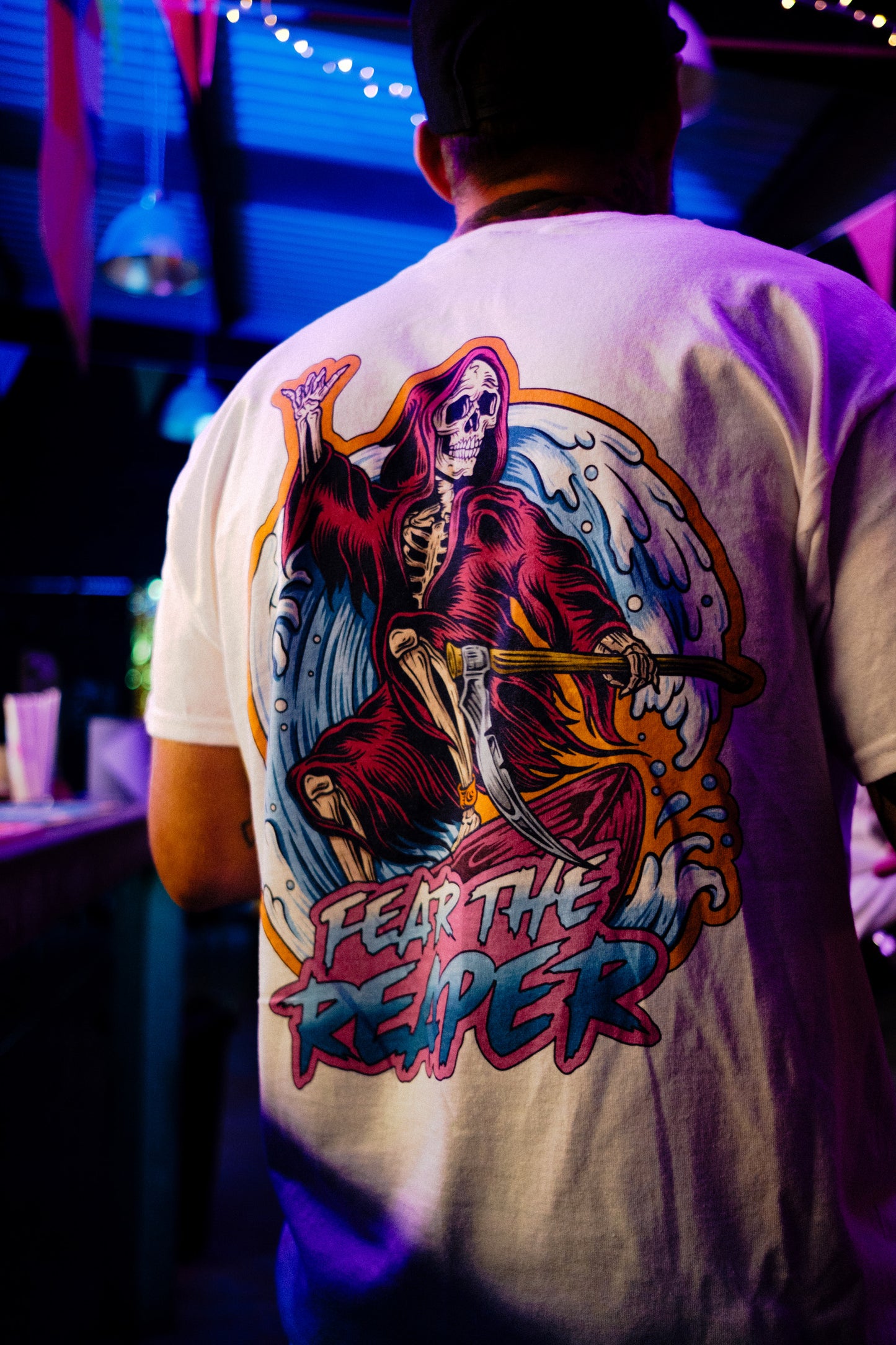 Person wearing a t-shirt with a graphic design of a skeleton holding an axe and text 'FEAR THE REAPER' in a club setting.