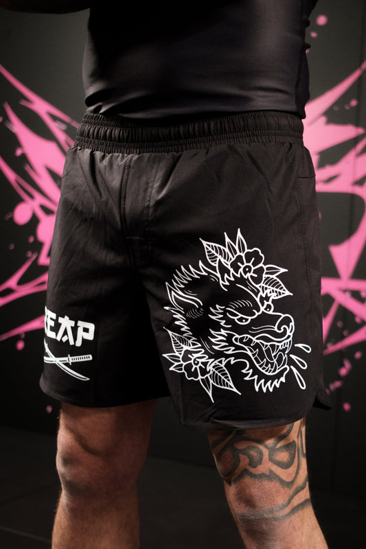 Black shorts with white dragon design and brand logo on a dark background with pink abstract patterns.