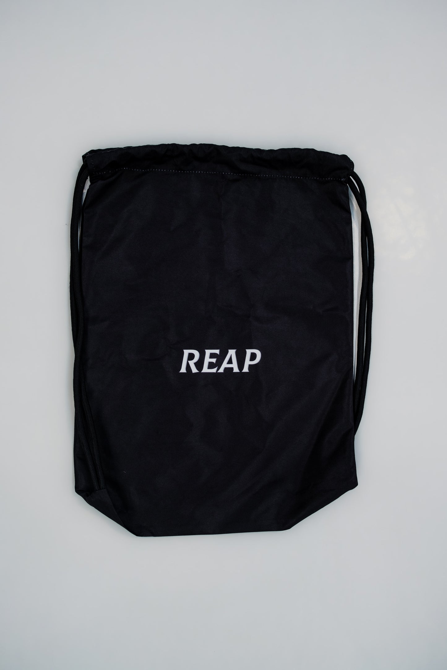 Black drawstring bag with 'REAP' text on a light gray background
