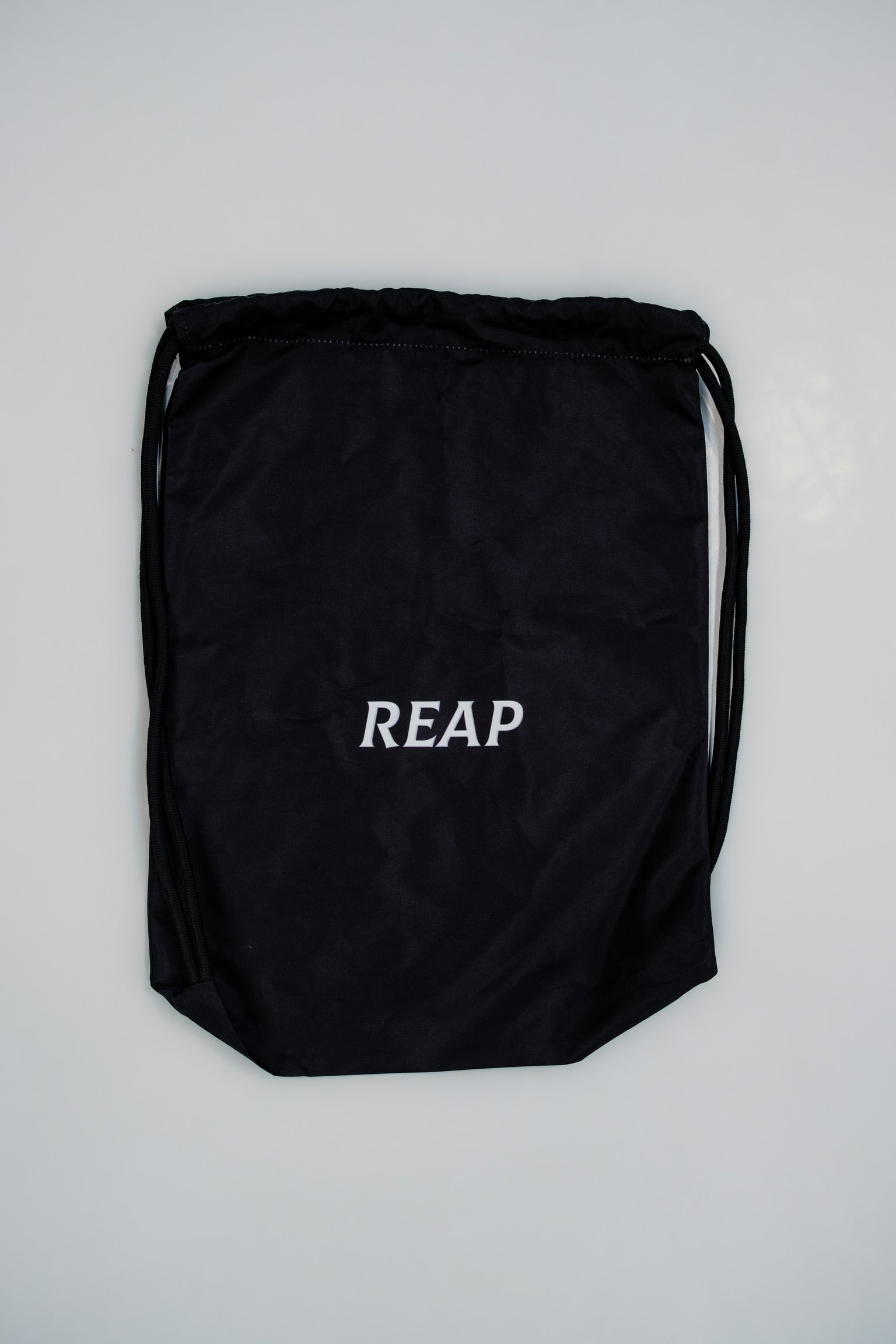 Black drawstring bag with 'REAP' text on a light gray background