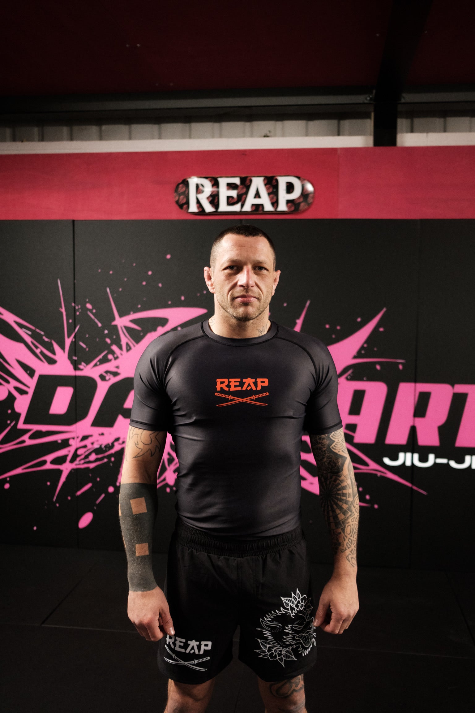 Person wearing a black 'REAP' athletic outfit in front of a red and black background with 'REAP' branding.