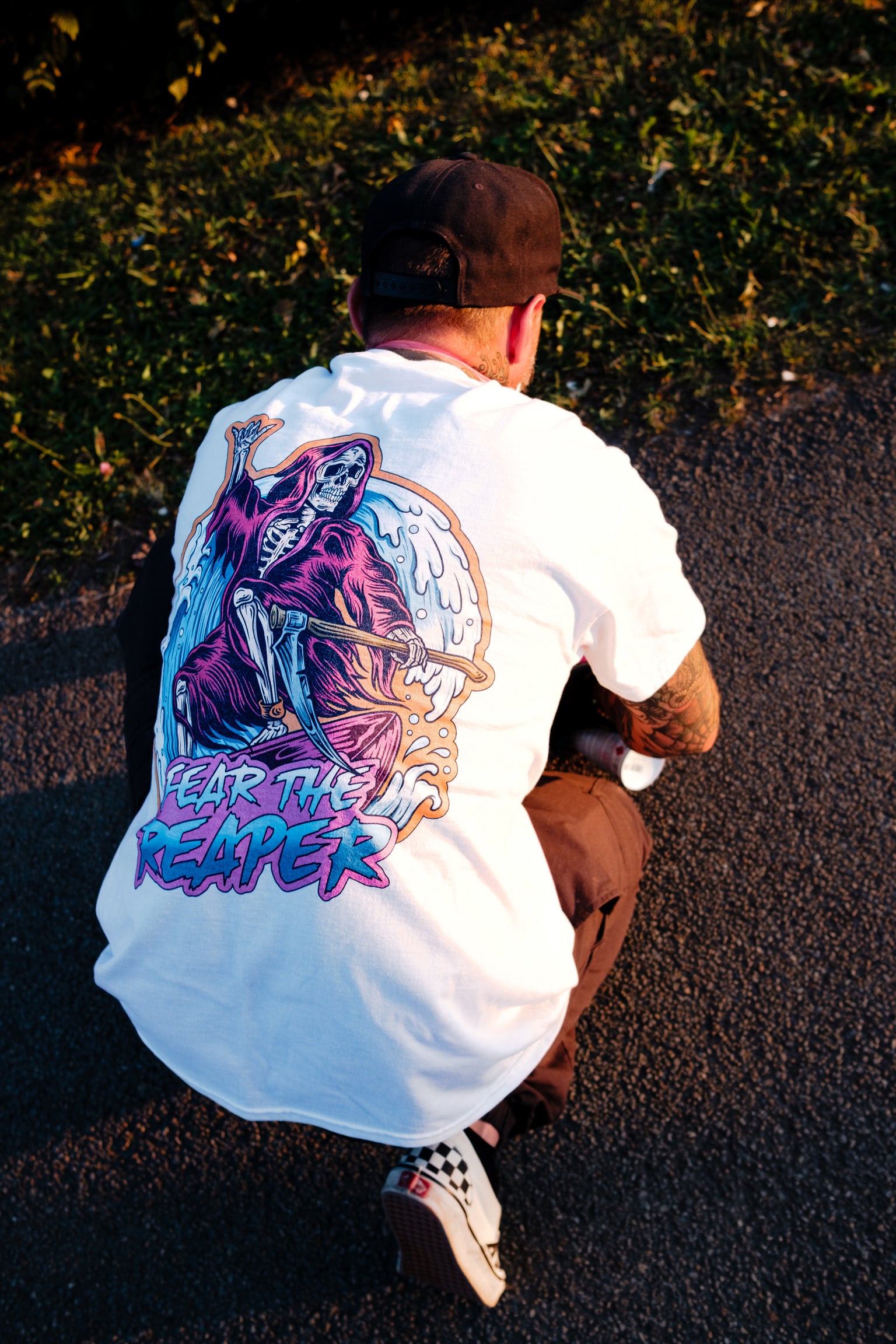 Person wearing a white t-shirt with a colorful graphic design on the back, sitting on a dark surface.