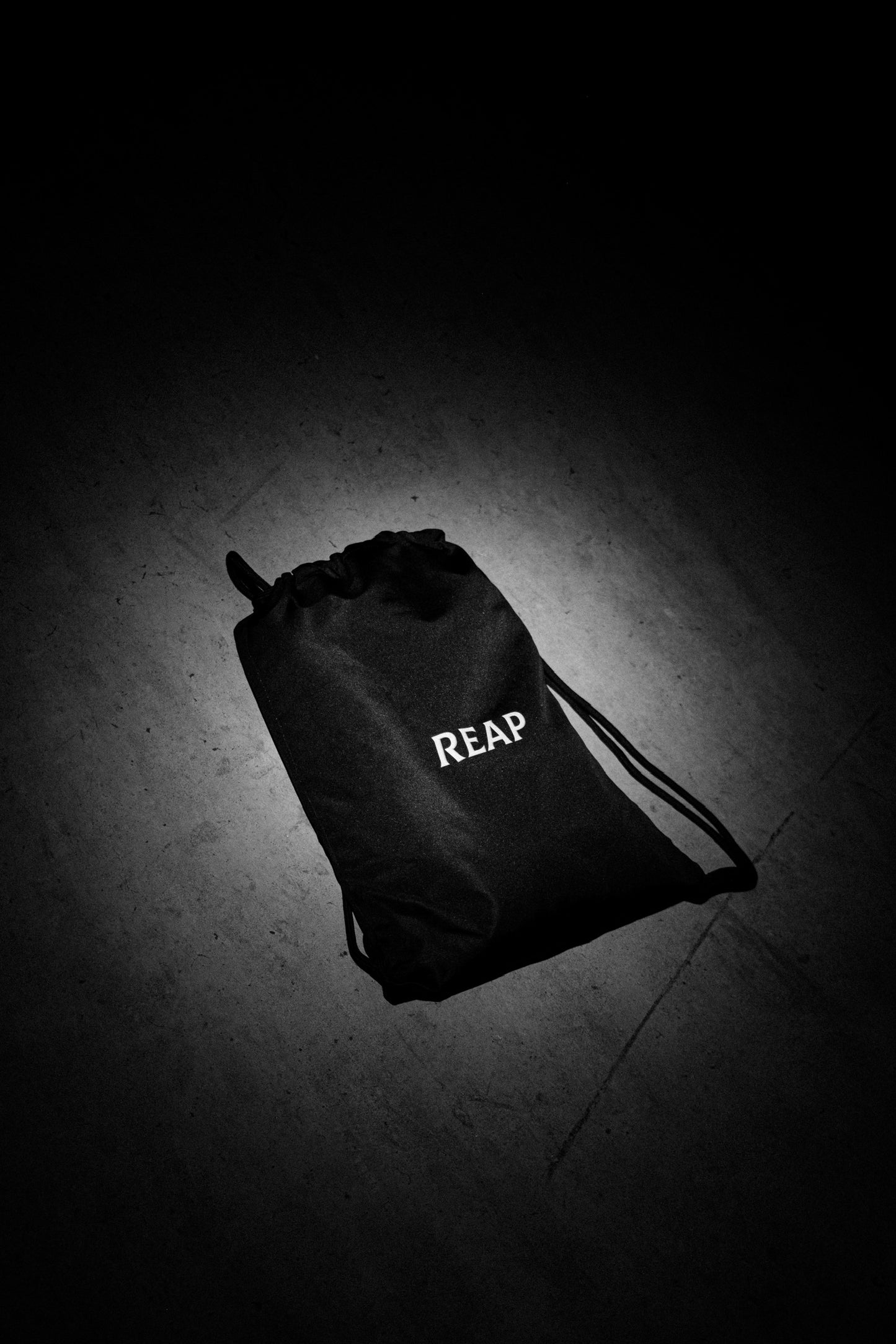 Black drawstring bag with 'REAP' branding on a dark floor.
