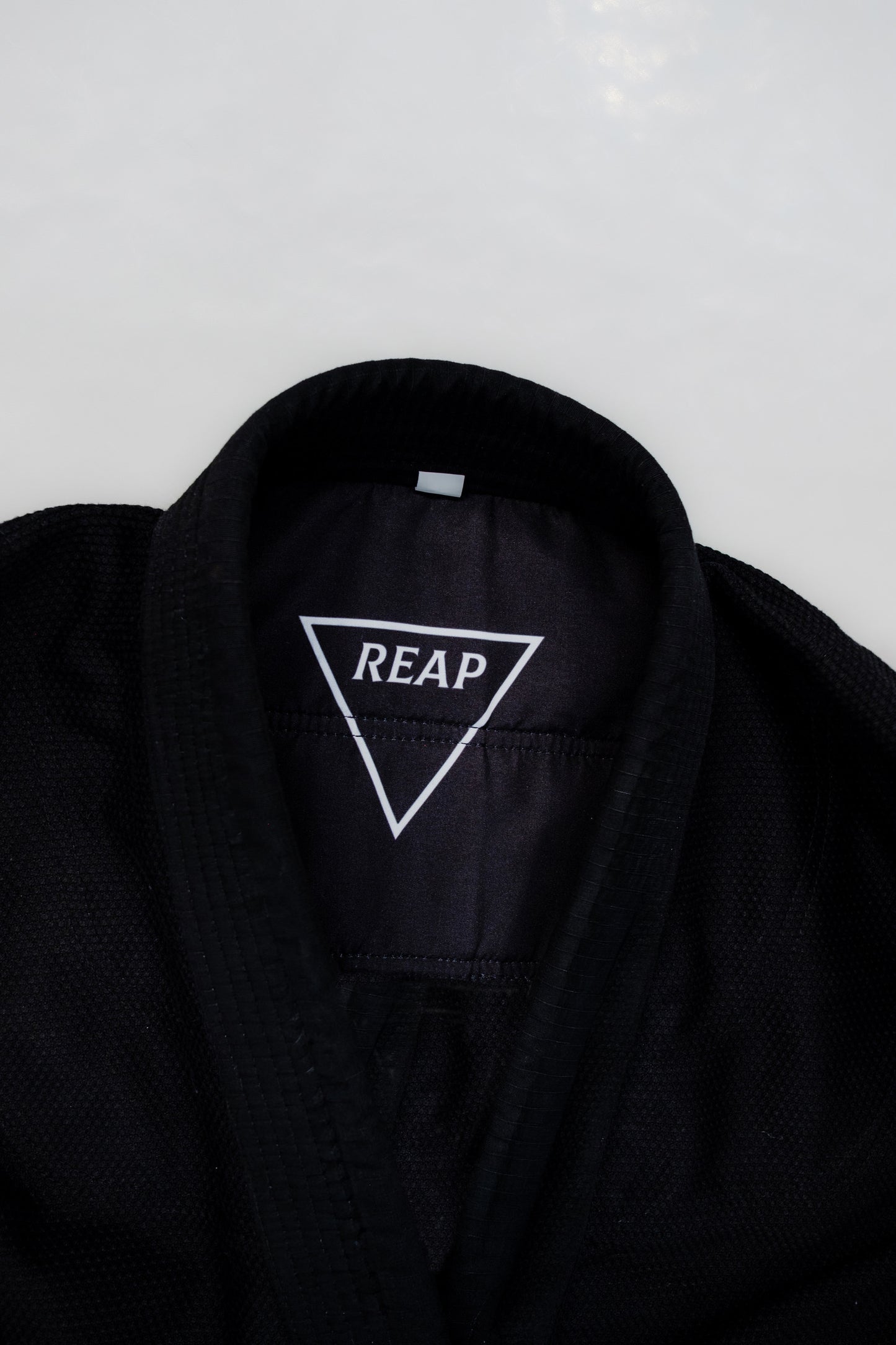 Black Gi jacket with 'REAP' logo on a white background