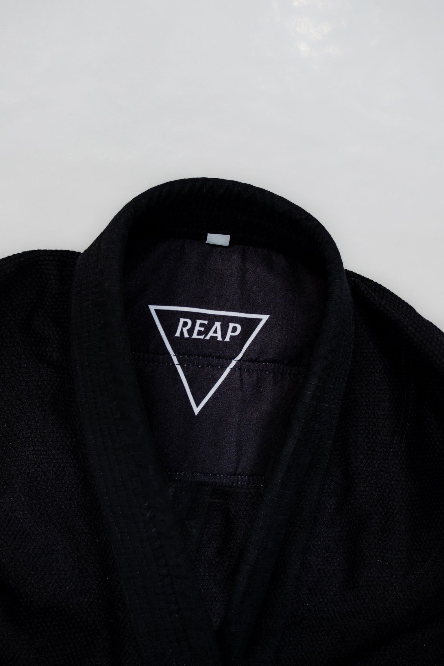 Black Gi jacket with 'REAP' logo on a white background